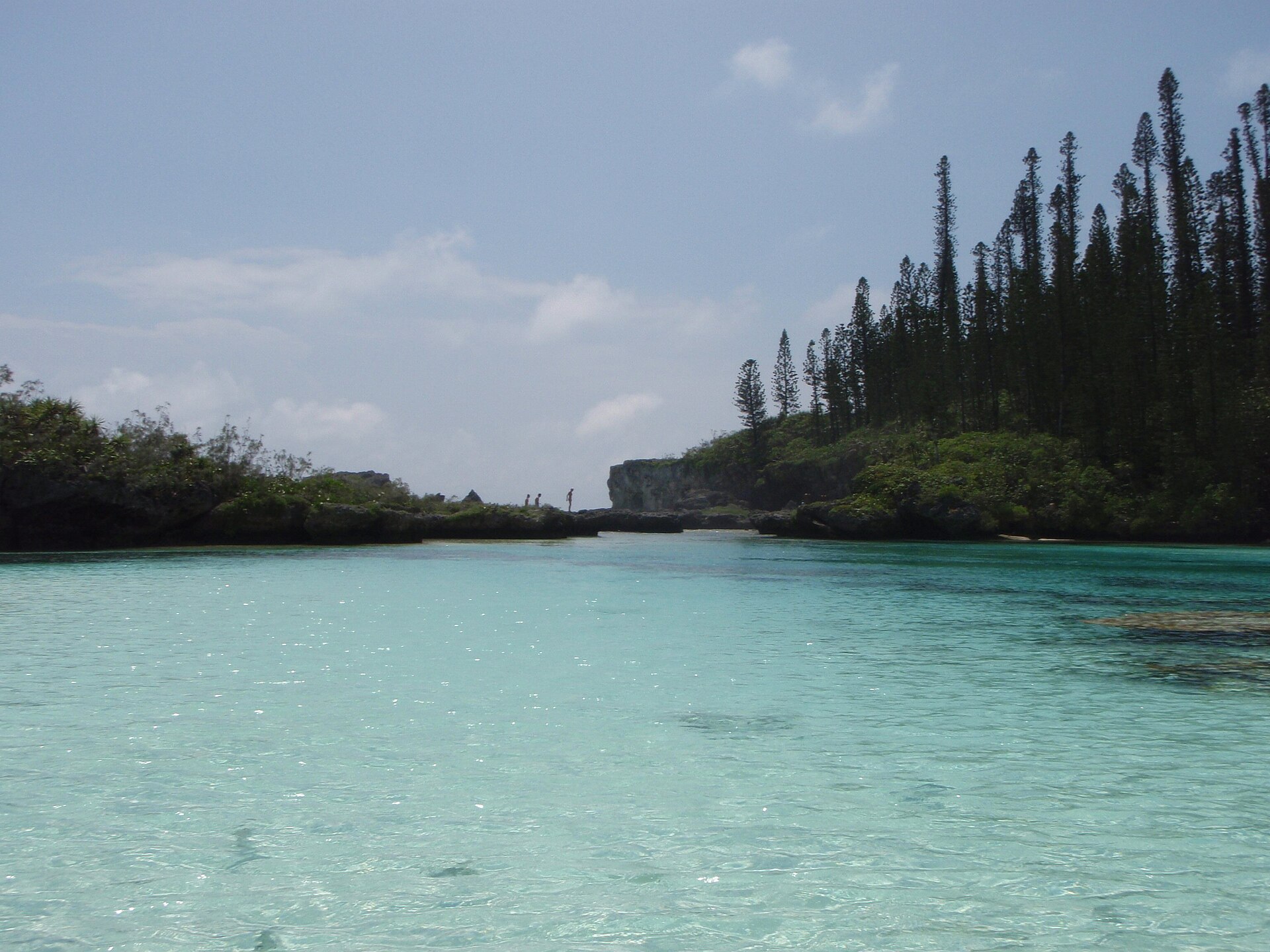 View of the natural aquamarine lagoon of Oro, Île des Pins, New Caledonia. In the center, the inlet feeding the lagoon with water from waves of the ocean. Tall trees are